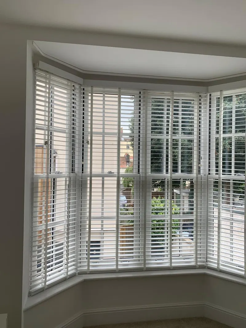 White wooden venetian blinds fitted across every pane of a bay window