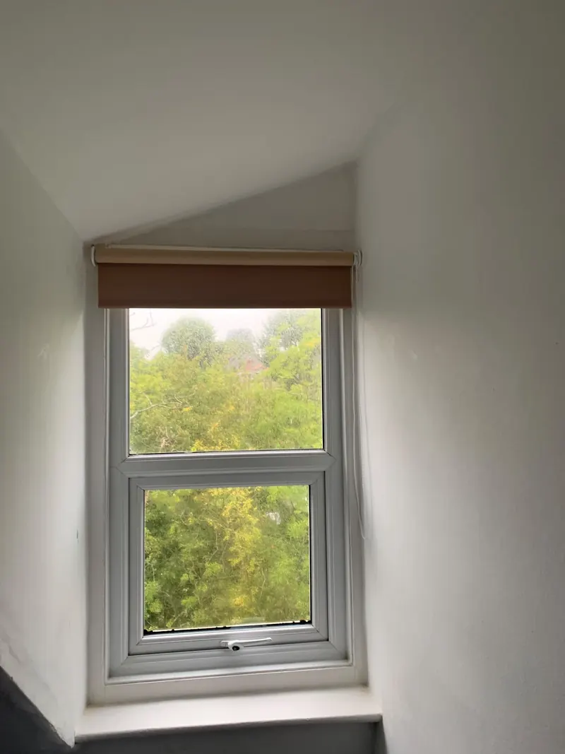 A roller blind fitted in the recess of a small window under a sloping ceiling